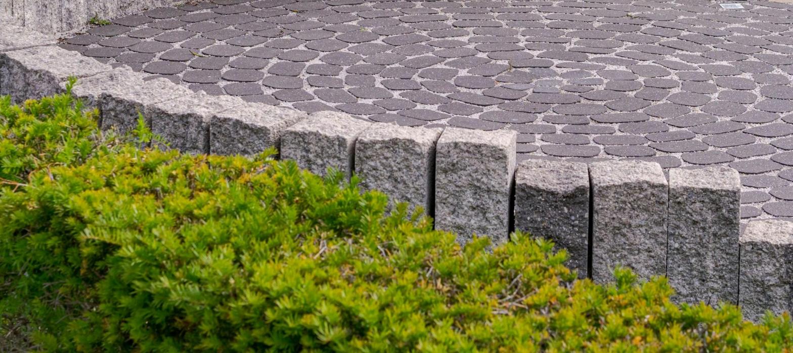 A circular paver patio edged with stone and low shrubs